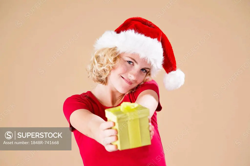 Smiling blond young woman wearing a Santa hat and presenting a gift