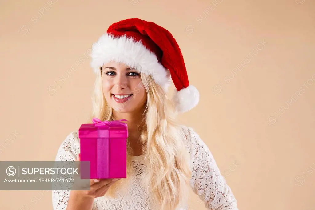 Smiling blond young woman wearing a Santa hat and presenting a gift