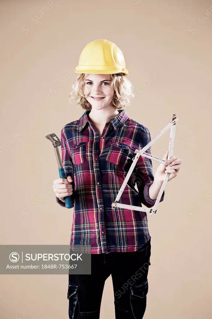 Girl holding a hammer and a wooden ruler folded in the shape of a house