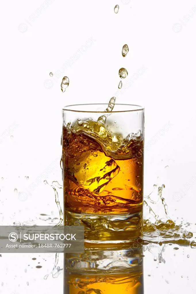 Ice cube falling into a whiskey glass with a splash