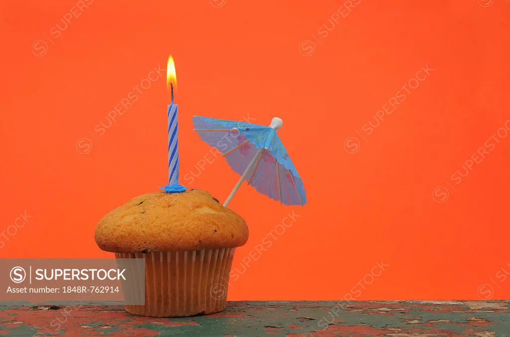 A muffin with a birthday candle and an umbrella