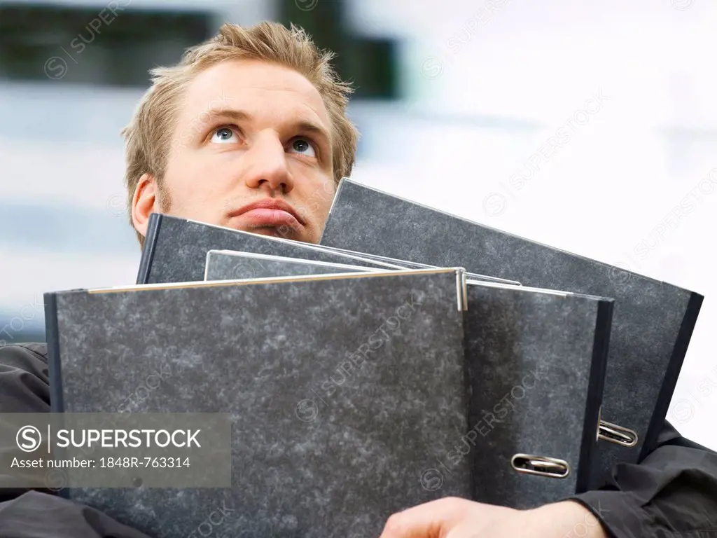 Businessman carrying ring binders, looking dissatisfied, frustrated