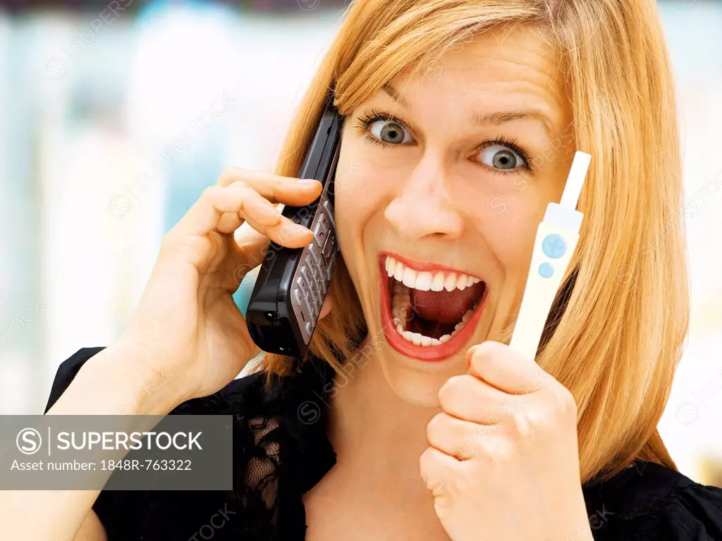 Woman holding a pregnancy test, using a telephone, happy