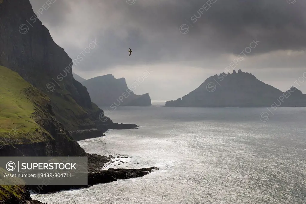 Cliffs in front of the silhouette of the rugged rocks of Tindhólmur, Vágar, Faroe Islands, Denmark