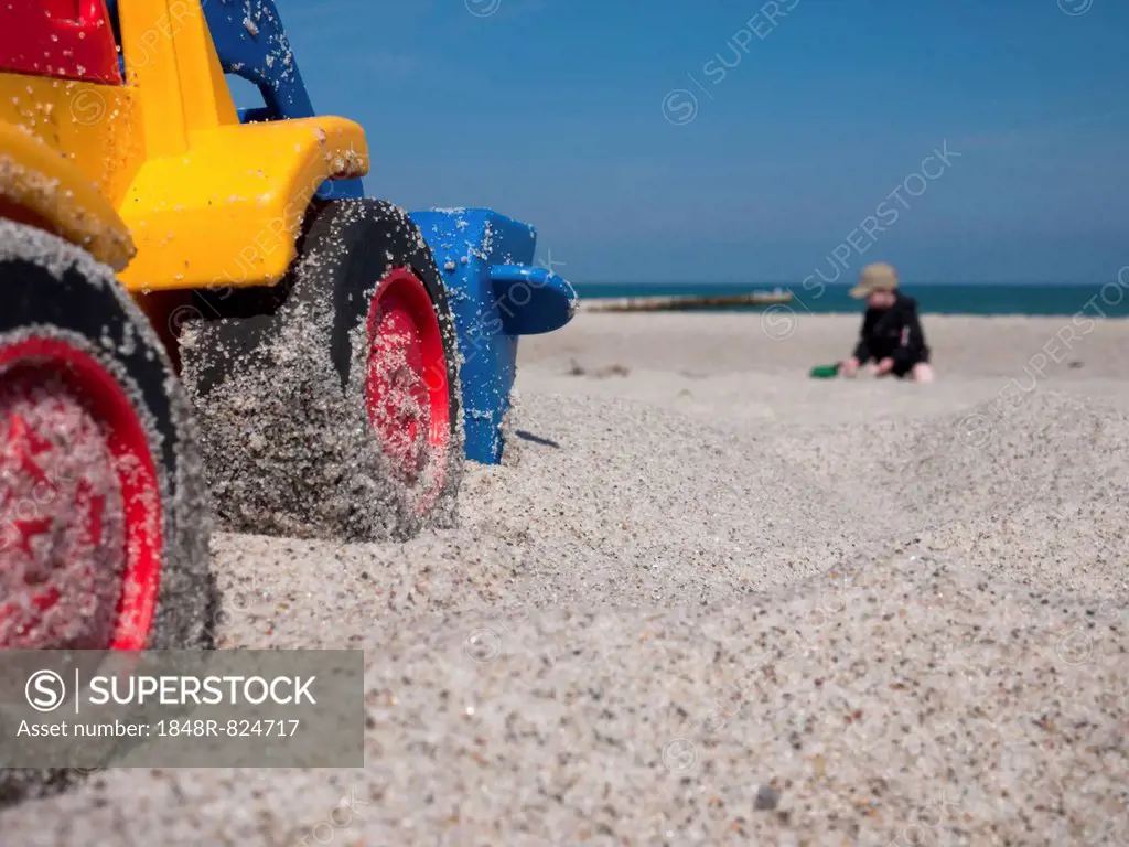 Toy digger on a beach, child at the back, Mecklenburg-Western Pomerania, Germany