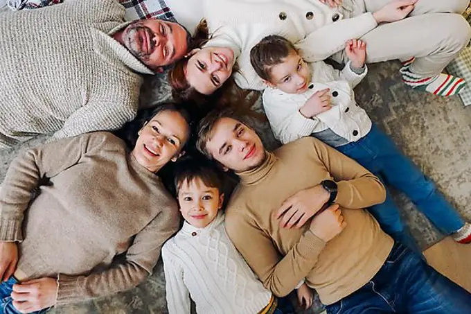 Top view of happy big multi-generation family lying in circle on floor and smiling at camera, strengthening bonds and building healthy relationships right from childhood. Family love and unity