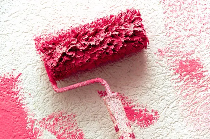 Paint roller with pink paint on a white wall