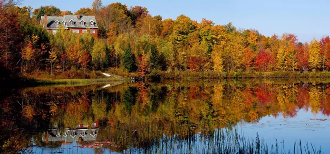 House on beaver pond amongst the trees in autumn, Eastern Townships, West Bolton, Quebec, Canada