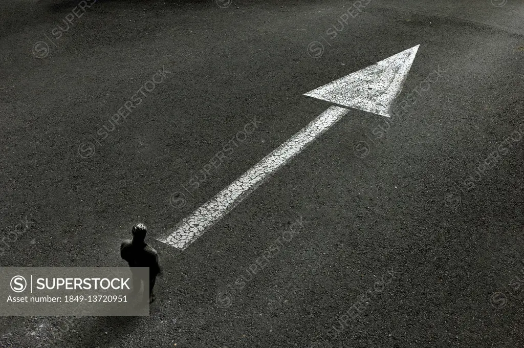 Man standing looking at arrow painted on road pointing the way ahead