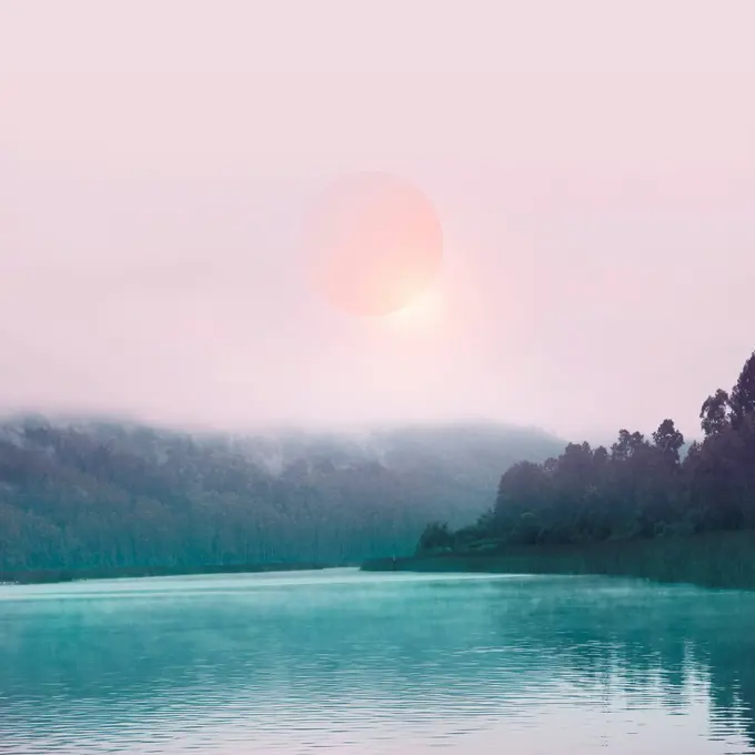 Pink sun in mist above lake