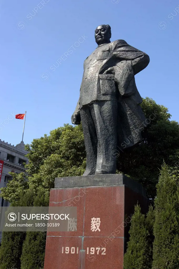 China, Shanghai, The Bund. Statue Of Mao Against A Backdrop Of Formal Bushes And A Flag Fly From The Roof Of The Building In The Background