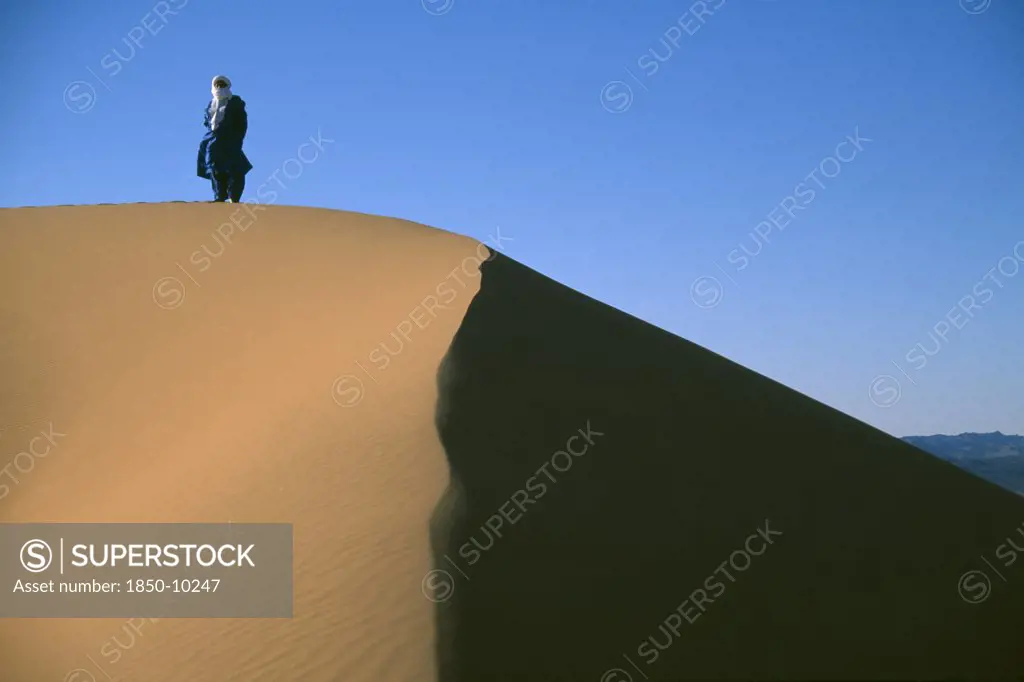 Libya, Sahara Desert, Tuareg Man Standing On Ridge Of Sand Dune.
