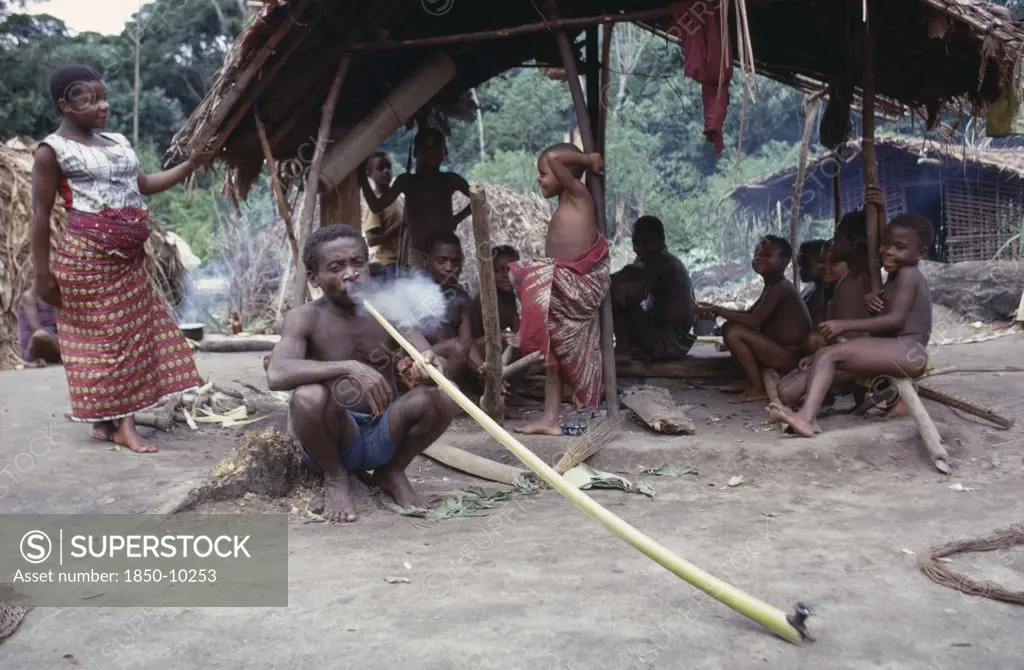 Congo, Ituri Forest, Pygmy Group With Man Smoking Hallucinogens In Long Pipe.