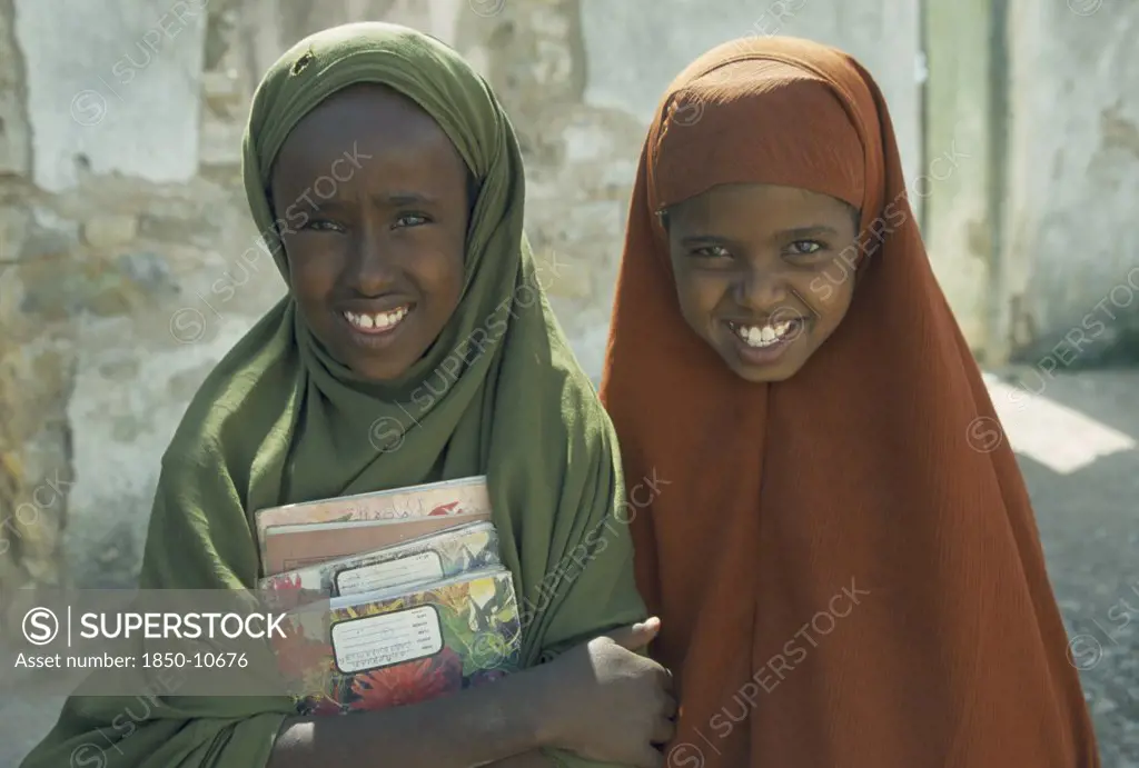 Somalia, Baidoa, Portrait Of Two Schoolgirls With Covered Heads Carrying School Books.