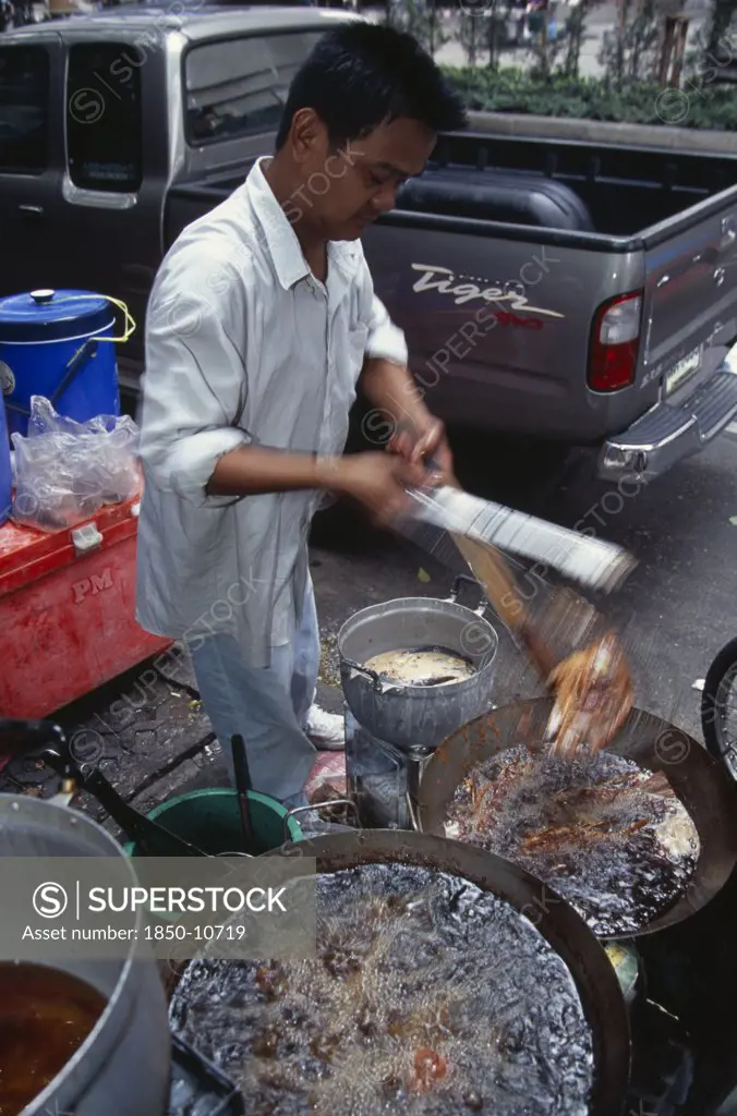 Thailand, South, Bangkok, Thanon Silom Male Vendor At His Stall On The Pavement Deep Frying Fish In Woks