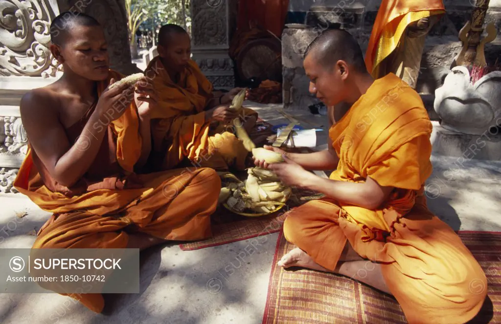 Cambodia, Siem Reap Province, Angkor Thom, Buddhist Monks Eating Steamed And Boiled Corn Donated By Elderly Lady.