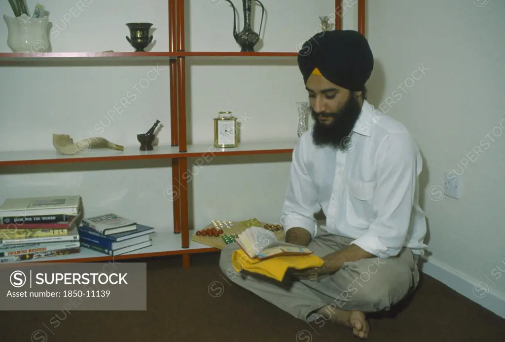 England, Religion, Skihism, Sikh Man Sitting On The Floor Of His Home Reading Gutka An Abbreviated Version Of The Guru Granth Sahib Scripture.