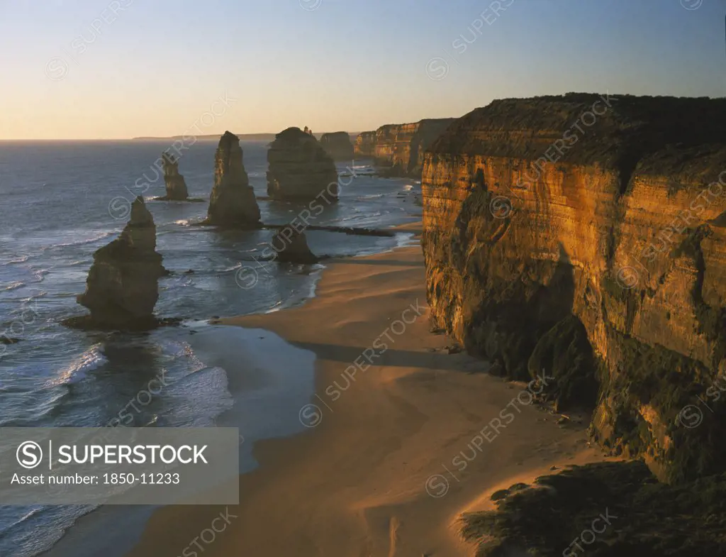 Australia, Victoria, Port Campbell N.P, Great Ocean Road. View Along The Beach And Cliffs Toward The Twelve Apostles Sea Stacks In Warm Evening Light