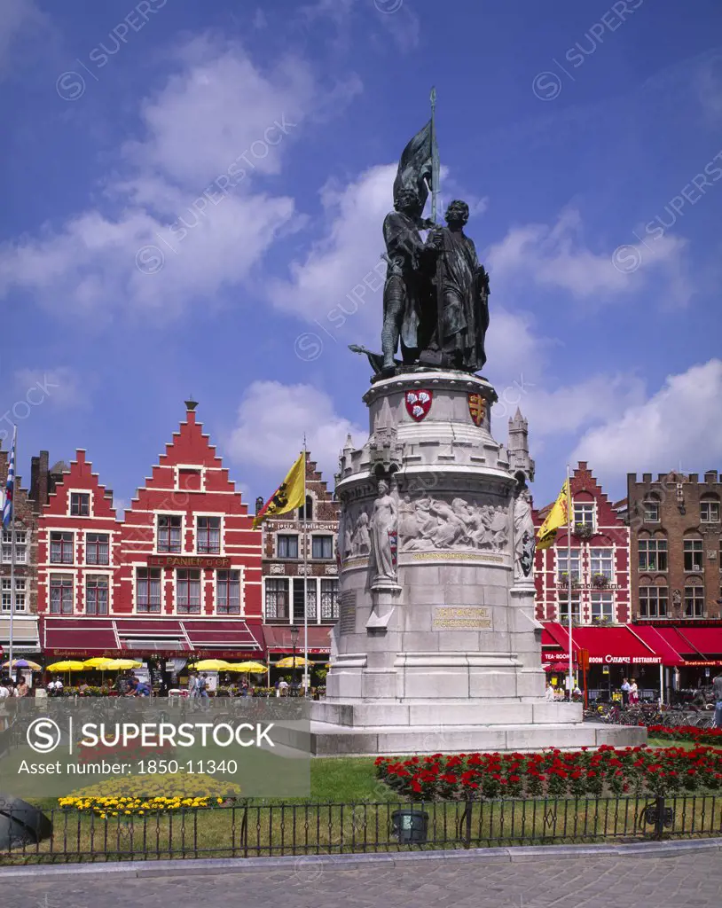 Belgium, West Flanders, Bruges, Statue Of Jan Breydel And Pieter De Coninck In The Market Place. Row Of Cafes And Restaurants Behind.