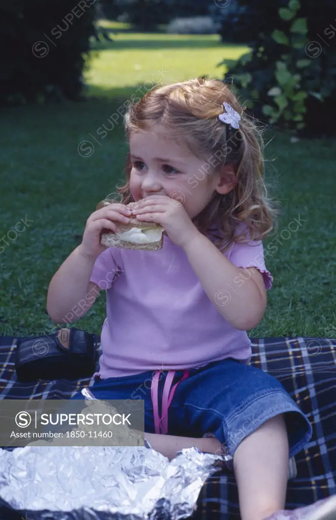 England, West Sussex, Chichester, The Bishops Palace Gardens.  Girl Aged Three Eating Brown Bread And Lettuce Sandwich During Picnic Lunch.