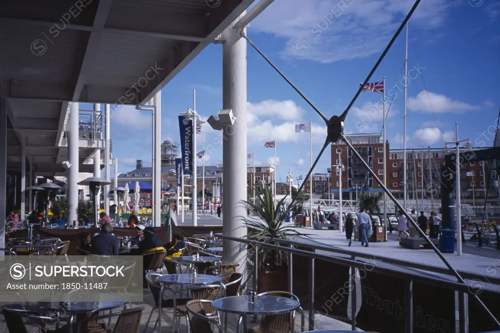 England, Hampshire, Portsmouth, 'Gunwharf Quay Shopping Centre. Outside Cafe With View Across Table, Chairs And Exterior Structures. '