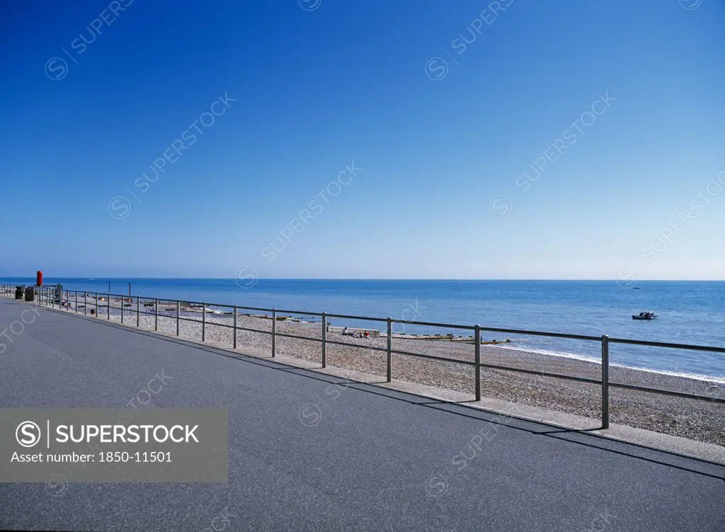 England, East Sussex, Bexhill On Sea, View From Path Across Railings Towards Shingle Beach And Calm Blue Sea.