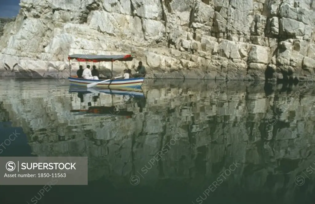 India, Madhya Pradesh, Marble Rocks, Painted Tourist Boat On The Narmada River Passing Sheer Cliffs Reflected In Water.