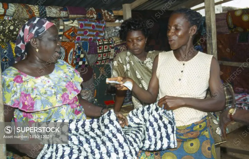 Ghana, West, Markets, Woman Purchasing Length Of Batik Dyed Cloth With Fish Design From Market Vendor.