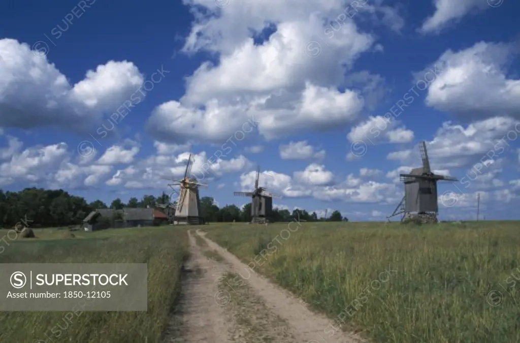 Estonia, Saaremaa Island, Dirt Track Leading To Windmills In Agricultural Landscape With Dramatic Cloudscape Above.