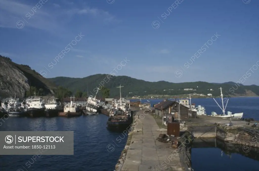 Russia, Siberia, Lake Baikal, Fishing Boats Moored Against Stone Jetty In Lake Harbour.