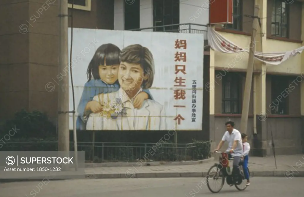 China, Shandong, Jinan, Man With Child Passenger Cycling Past Birth Control Poster With Image Of Female Child.