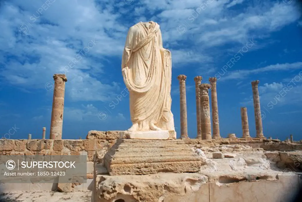 Libya, Tripolitania, Sabratha, Headless And Armless Classical Statue On Raised Plinth With Standing Columns Behind