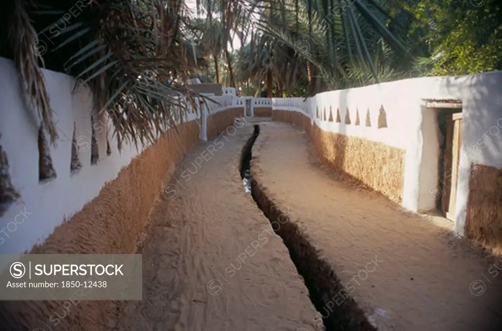 Libya, Ghadames, Deep Irrigation Channel Through Street Between Walls Partly Painted White With Triangular Cut Outs.