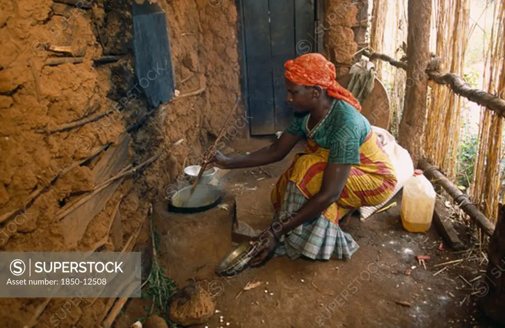 Tanzania, West, Great Lakes Region, Refugee Woman Cooking On Wood Saving Clay Stove Inside Hut With Mud Brick Walls.