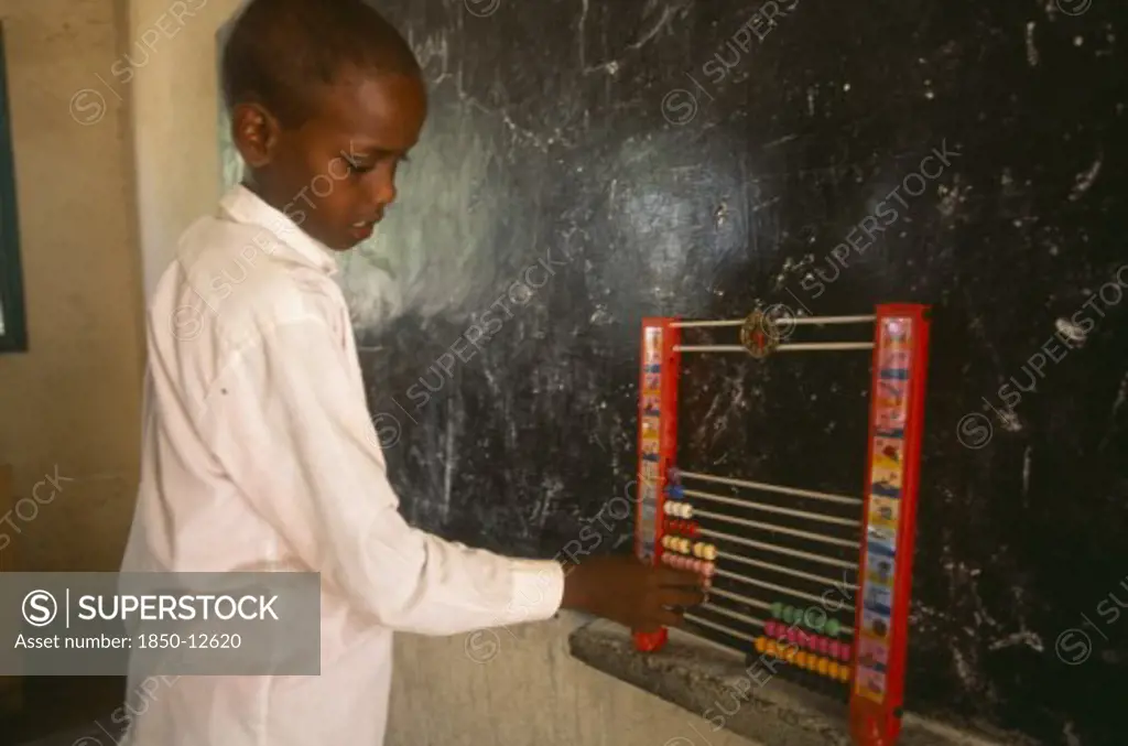 Somaliland, Hargeisa, Boy Using An Abacus In School Classroom With Blackboard On Wall Behind.