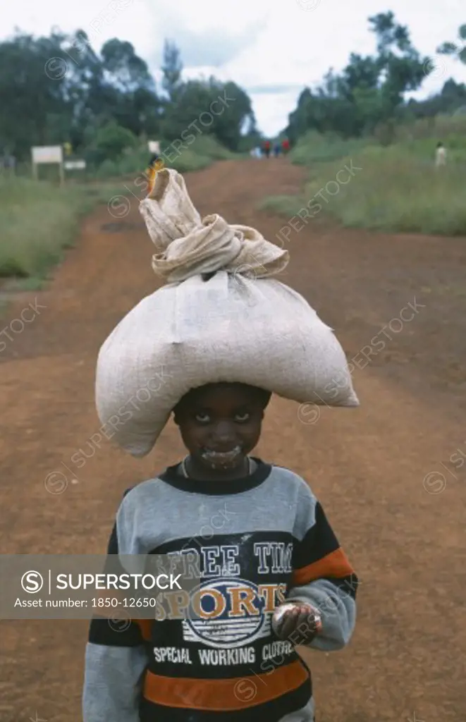 Tanzania, West, Great Lakes Region, Young Refugee Girl Carrying Sack Of Food On Her Head With Remnants Of Food All Around Her Mouth.