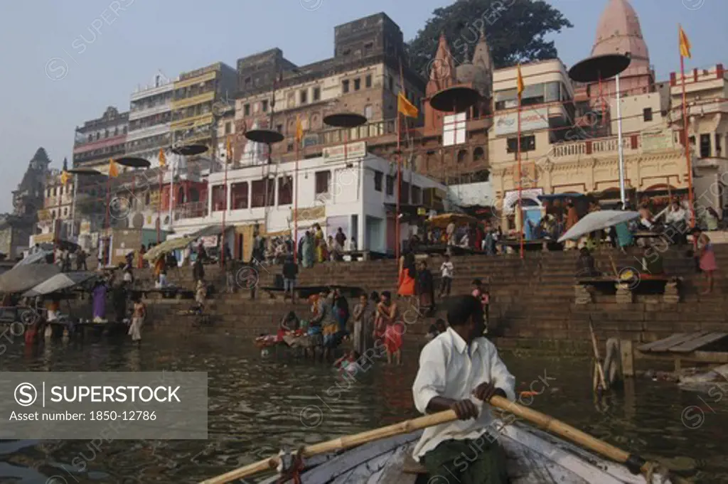 India, Uttar Pradesh, Varanasi, A Boatman Bringing His Boat Into Dashaswamedh Ghat With Early Morning Bathers In The Ganges River