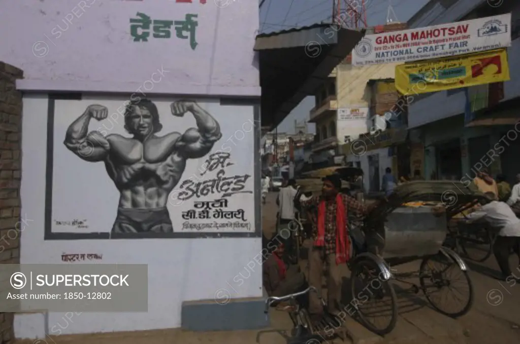India, Uttar Pradesh, Varanasi, A Young Arnold Schwarzenegger Painted On A Poster For Underwear With Rickshaw Driver Nearby