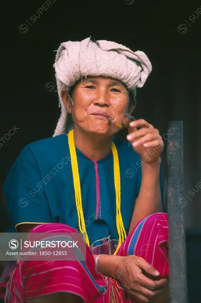 Thailand, Chiang Mai, Doi Inthanon National Park. Portrait Of A Karen Woman Sitting On The Steps Of Her House Smoking A Pipe