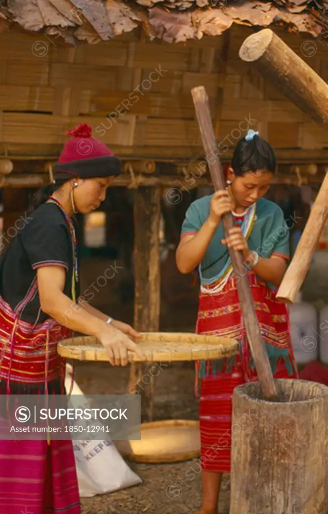 Thailand, Chiang Mai, Sgaw Karen Woman Pounding Rice By Hand While Another Sifts With A Large Bamboo Tray