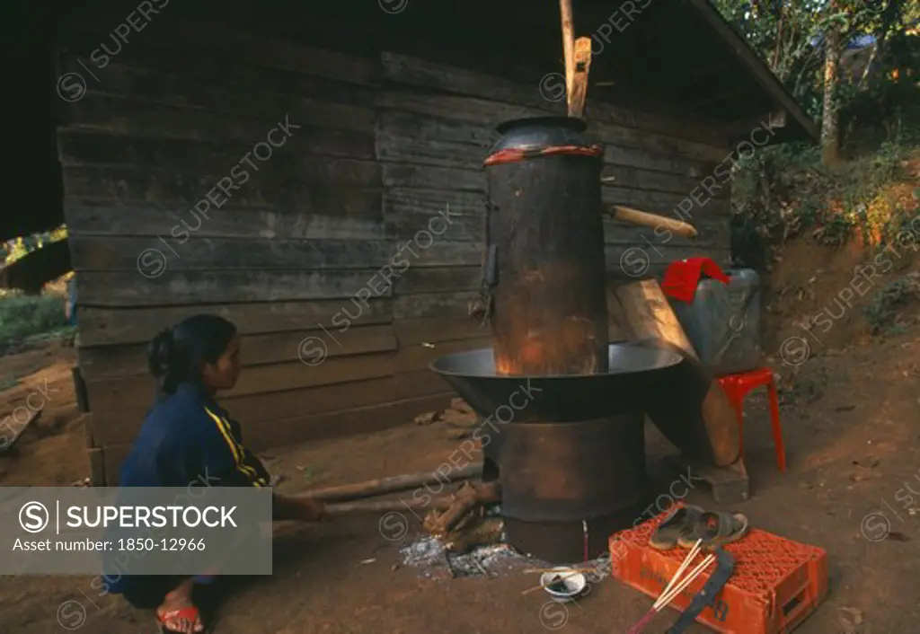 Thailand, Chiang Rai Province, Doi Lan, Lisu Woman Stoking Fire Of Her Still For Making Corn Whiskey