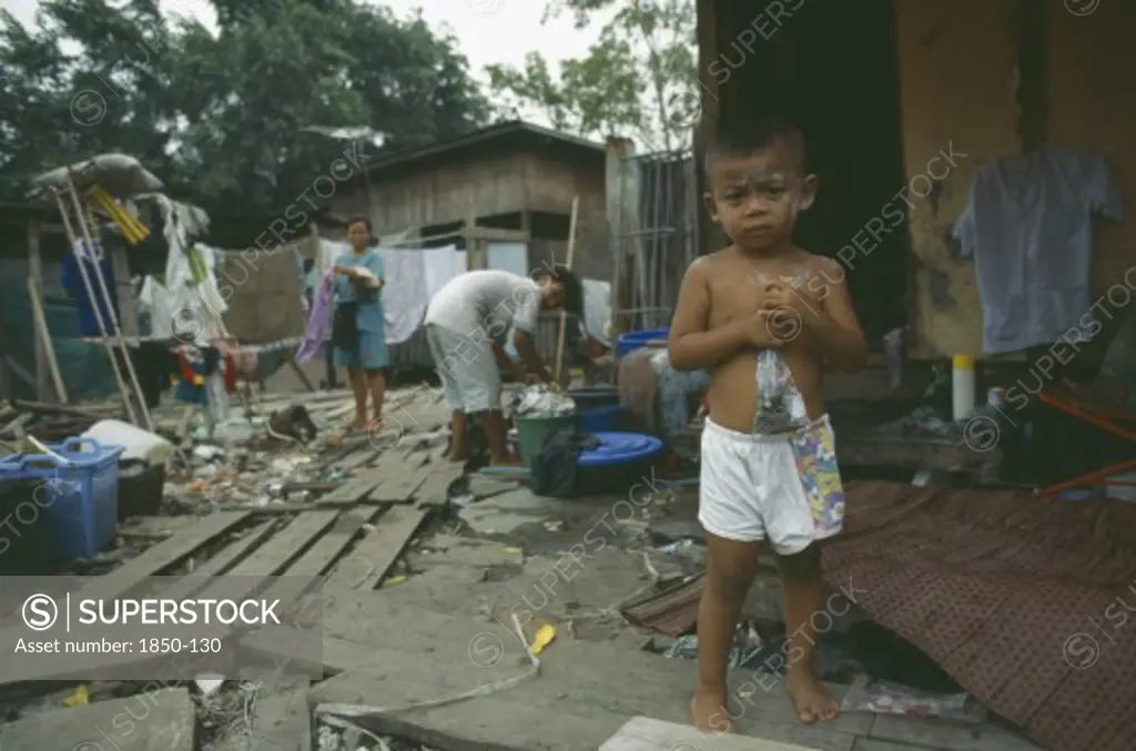 Thailand, Bangkok, Klong Toey. Child Standing By Women Hanging Washing In Slum Housing Area