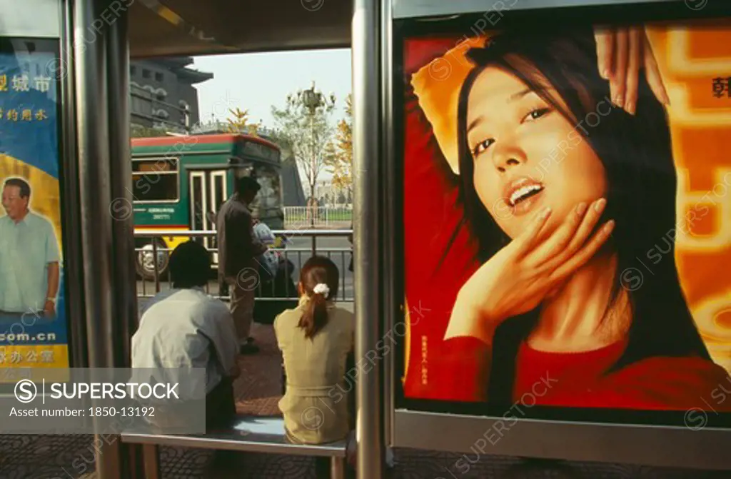 China, Beijing, People Waiting At Bus Stop South Of Tiananmen Square With Advertising Hoarding Covering Exterior Wall.