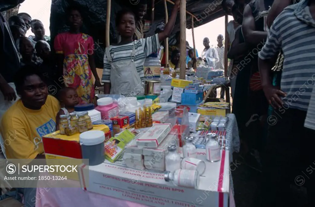 Liberia   , Nimba, Saclepea, Woman Behind Stall With Display Of Medical Supplies Surrounded By Crowd Of Adults And Children.