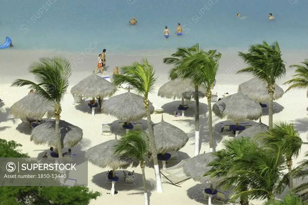 West Indies, Dutch Antilles, Aruba, View Looking Down On White Sandy Beach Lined With Thatched Umbrellas And Small Palm Trees