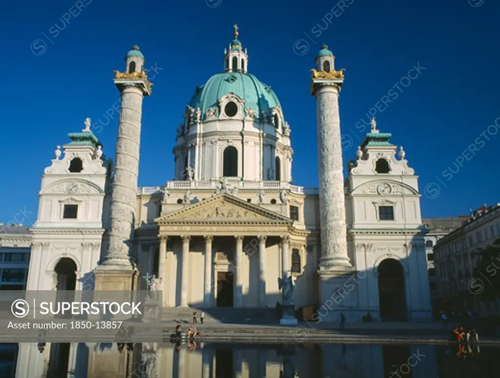 Austria, Vienna, Karlskirche Aka Church Of St Charles Borromaeus. View Of The Facade Showing Twin Columns And Domed Roof With Pool In The Foreground