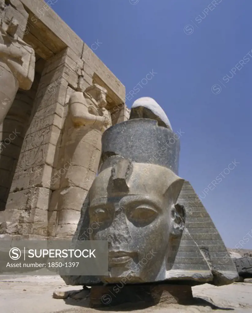 Egypt, Nile Valley, Thebes, 'The Ramesseum, Large Fallen Carved Stone Head Of Ramses Ii At Foot Of The Remains Of Osiride Columns Which Depict Ramses As Osiris, God Of The Underworld.'