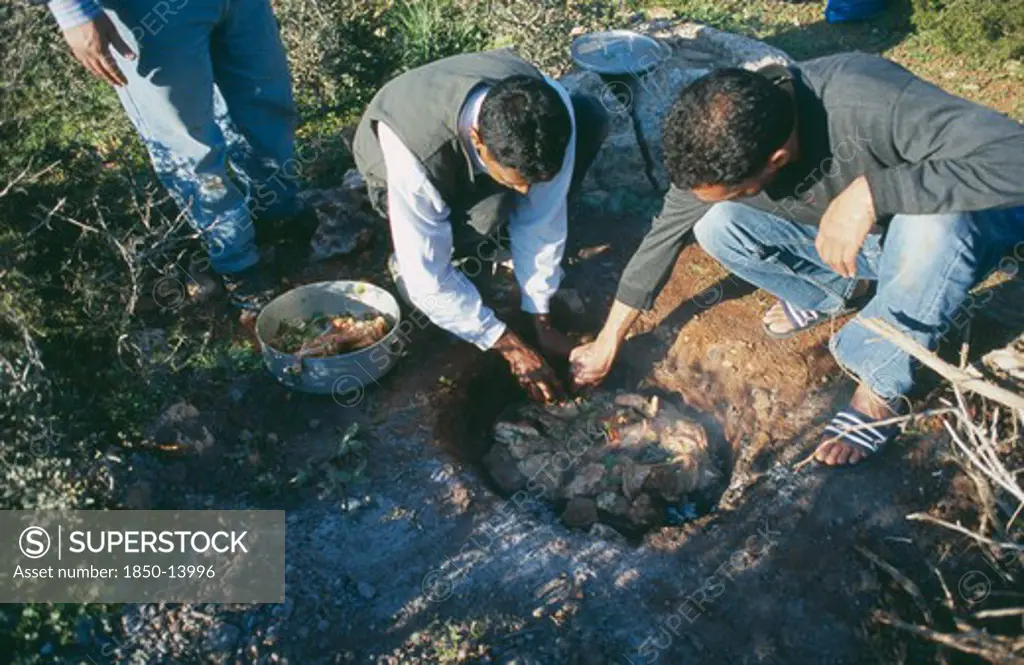 Libya, Cyranaica, Men Cooking Meat On Hot Stones In A Hole In The Ground.