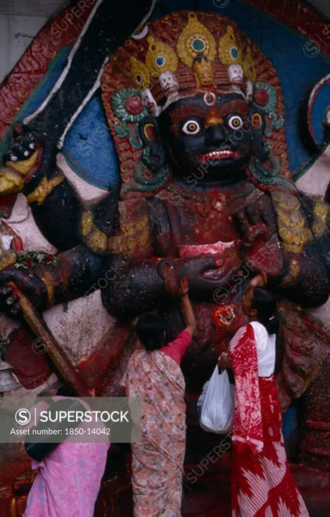Nepal,  , Kathmandu, Women Making Offerings At The Kala Bhairab Or Black Shiva In Durbar Square Representing The Fearsome Tantric Form Of Shiva In Nepal.