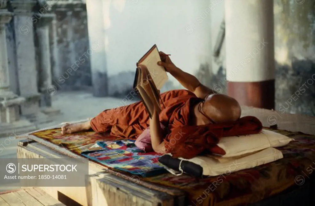 Myanmar, Yangon, Buddhist Monk Lying On Raised Platform And Reading In Shwedagon Pagoda.